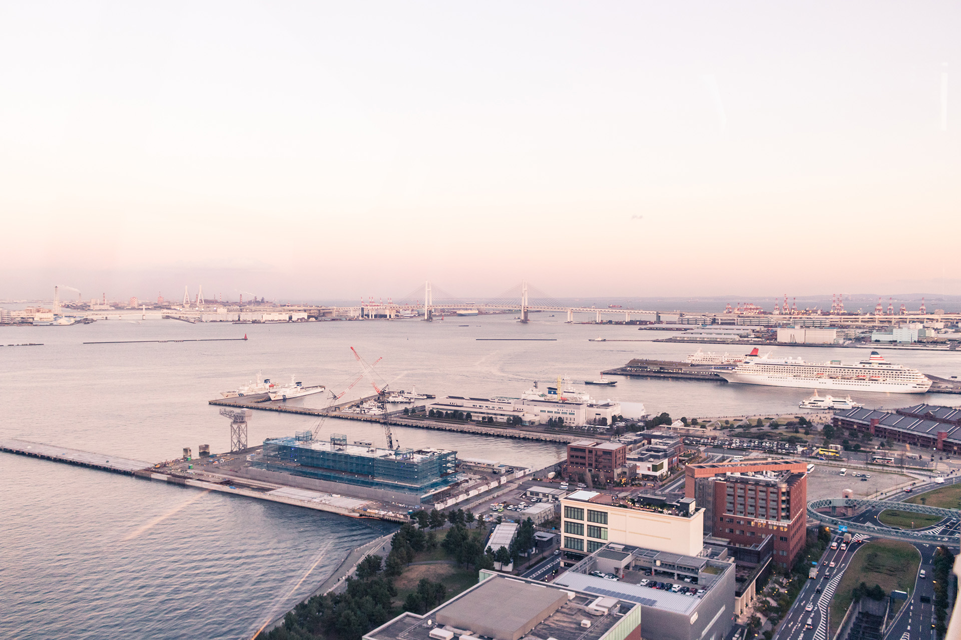 Wide bay surrounded by modern piers on its sides with a bridge crossing it in the distance, seen from a high vantage point.
